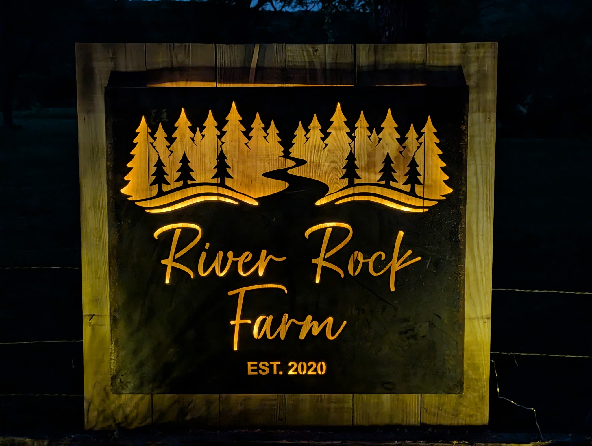 7628204745473872261 Illuminated sign, River Rock Farm logo, nighttime.